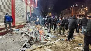 Protesters in Tehran holding banners and raising their fists amid heavy police presence during nationwide demonstrations in Iran, January 2026.