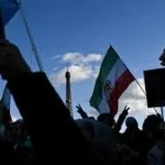Protesters in Tehran holding banners and raising their fists amid heavy police presence during nationwide demonstrations in Iran, January 2026.
