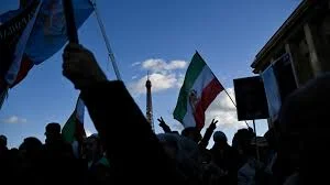 Protesters in Tehran holding banners and raising their fists amid heavy police presence during nationwide demonstrations in Iran, January 2026.