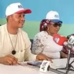 APC leaders seated at a press briefing table wearing party caps and addressing journalists